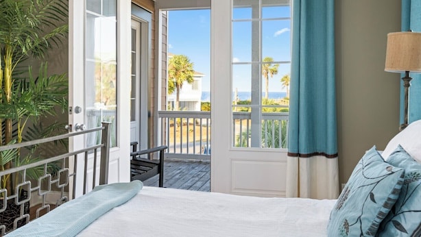 A bedroom with a view of the beach, a balcony with a chair, and a potted plant.