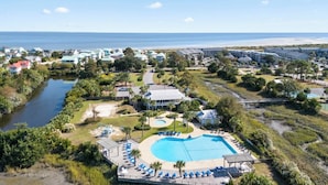 An aerial view of a resort with a central swimming pool, beachfront properties, and a body of water.