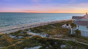 A coastal property with a beach view, a wooden deck, and a house with a porch.