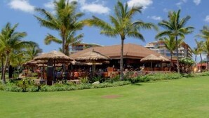 A resort with thatched umbrellas, palm trees, and a well-maintained lawn.