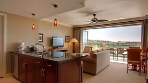 A hotel room with a kitchen area, a sofa, a dining table, and a balcony with a view.