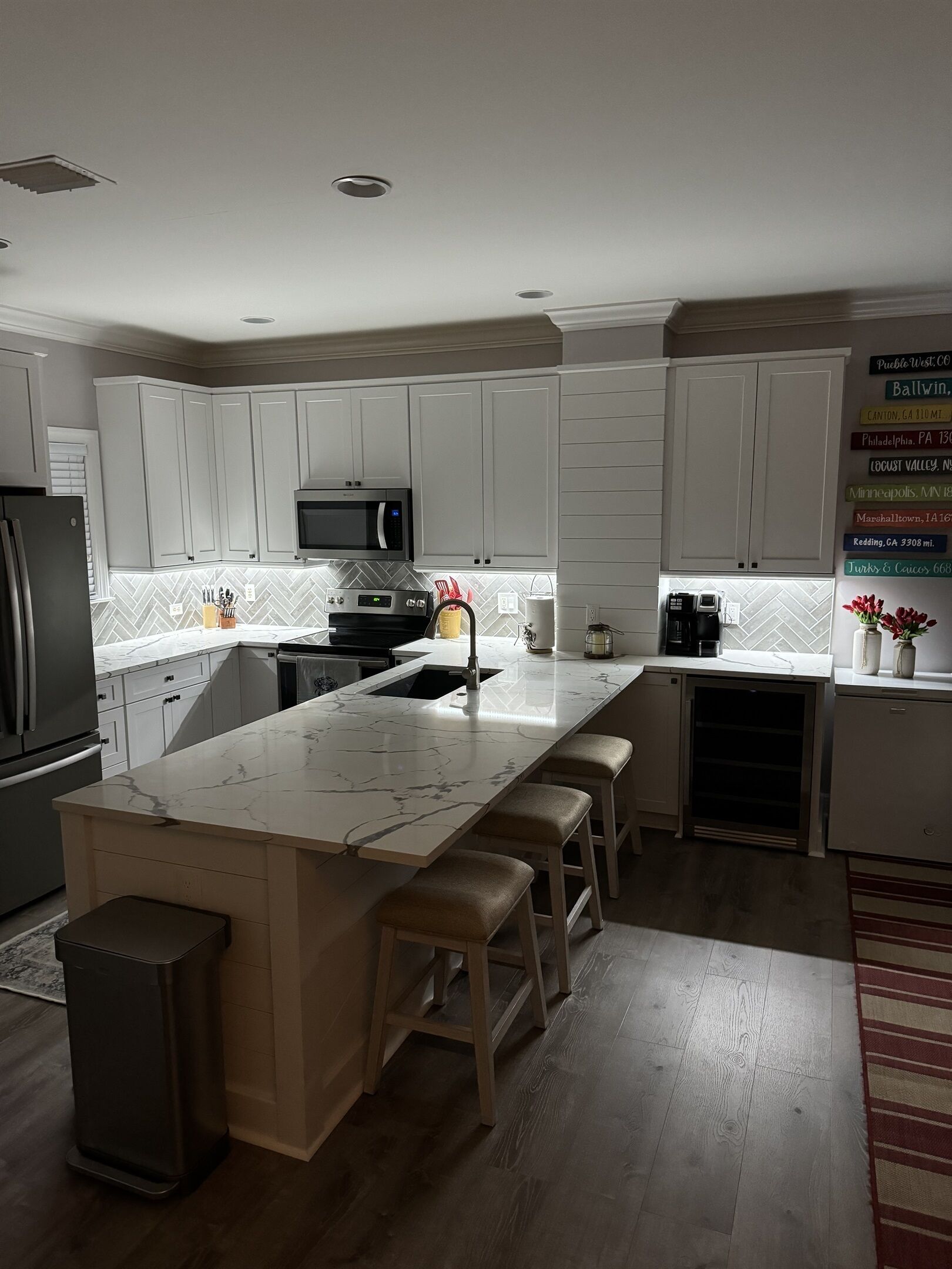 A modern kitchen with white cabinets, a marble island, and a stainless steel refrigerator.