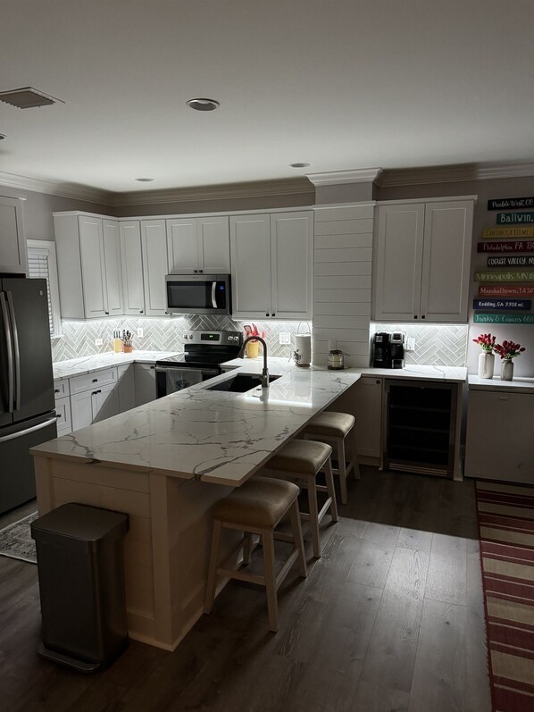 A modern kitchen with white cabinets, a marble island, and a stainless steel refrigerator.