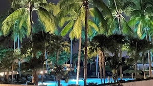 Vista nocturna de un resort con palmeras y una piscina.