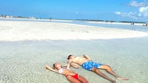 Dos personas descansando en una playa despejada con una zona de arena blanca al fondo.
