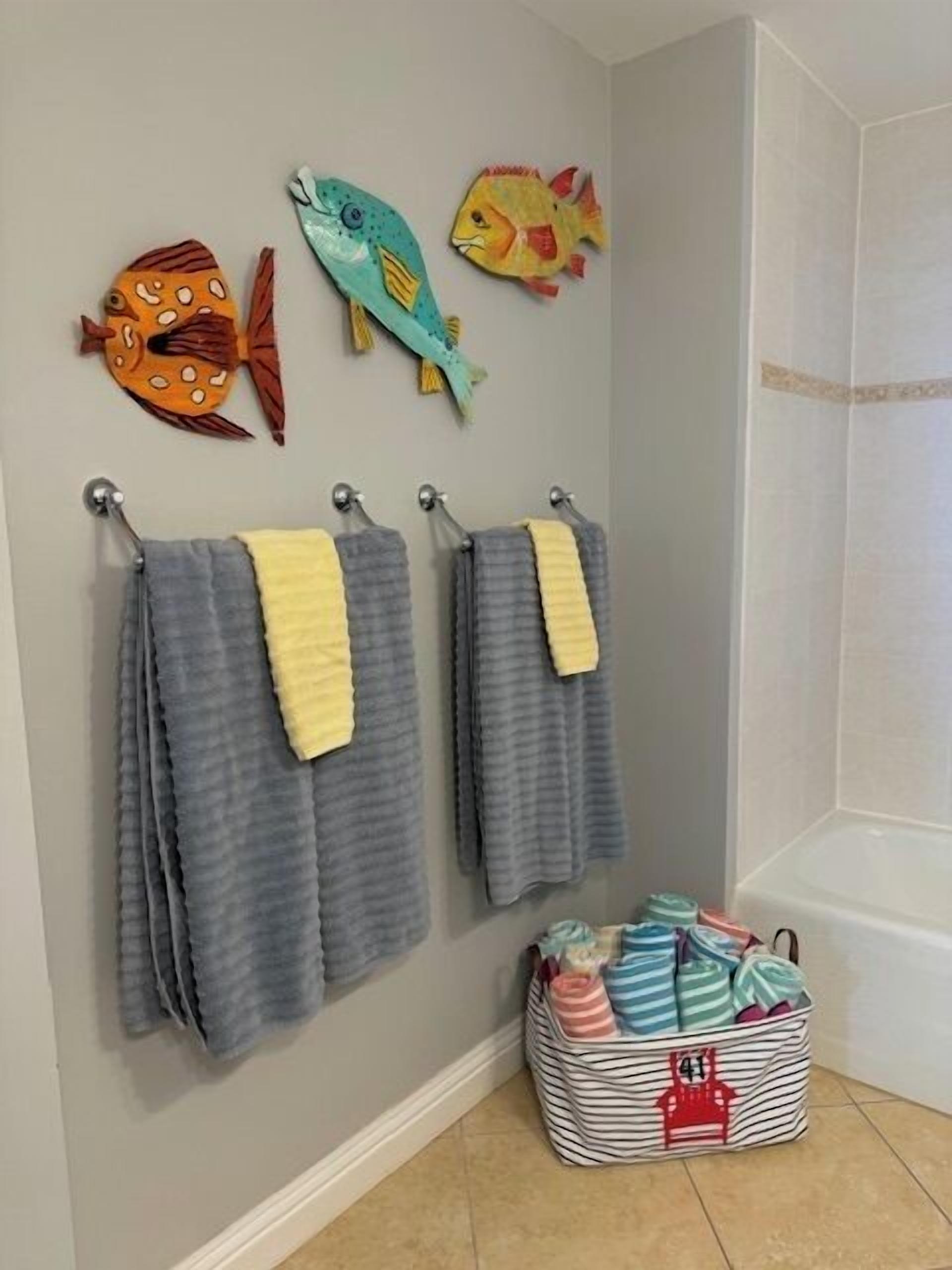 A bathroom with two towels hanging on hooks, a striped laundry basket, and three fish-shaped wall decorations.