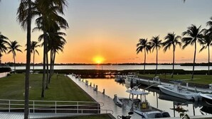 Un puerto deportivo con barcos amarrados, palmeras y un atardecer de fondo.
