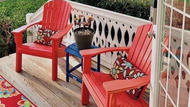 Un porche con dos sillas Adirondack rojas y una silla azul, una planta en maceta y vistas a un campo de golf y al agua.