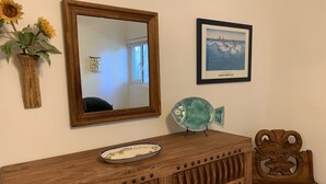 Un aparador de madera con espejo, un cuadro enmarco, un pez decorativo y una silla.