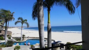 Zona de piscina con palmeras, vista a la playa y cielo despejado.