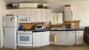 Una cocina compacta con armarios blancos, microondas, tostadora, hervidor y pileta.