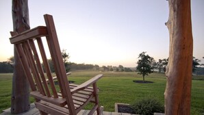 Une chaise en bois sur une terrasse, avec vue sur un champ verdoyant et des arbres.