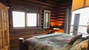 A log cabin bedroom with a wooden bed, a window with blinds, a nightstand with a lamp, and a wooden wardrobe. - Johnson's Country Cabin - One price rents the entire home! (Afton)