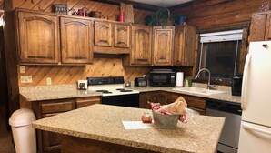 A kitchen with wooden cabinets, granite countertops, a stainless steel refrigerator, and a granite island with stools. - Johnson's Country Cabin - One price rents the entire home! (Afton)