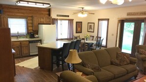 A cozy living room with a sofa, a coffee table, and a dining area with chairs and a table. There is a kitchen with wooden cabinets and a refrigerator. - Johnson's Country Cabin - One price rents the entire home! (Afton)