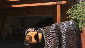 A wooden house with a balcony, a garage, and a bear sculpture in front.