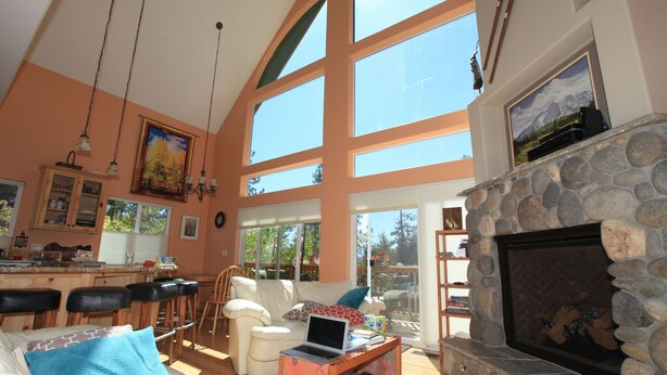 A spacious living area with a stone fireplace, large windows, and a kitchen area with bar stools.