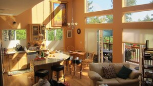 A spacious living area with a kitchen, dining table, and a large window overlooking a garden.