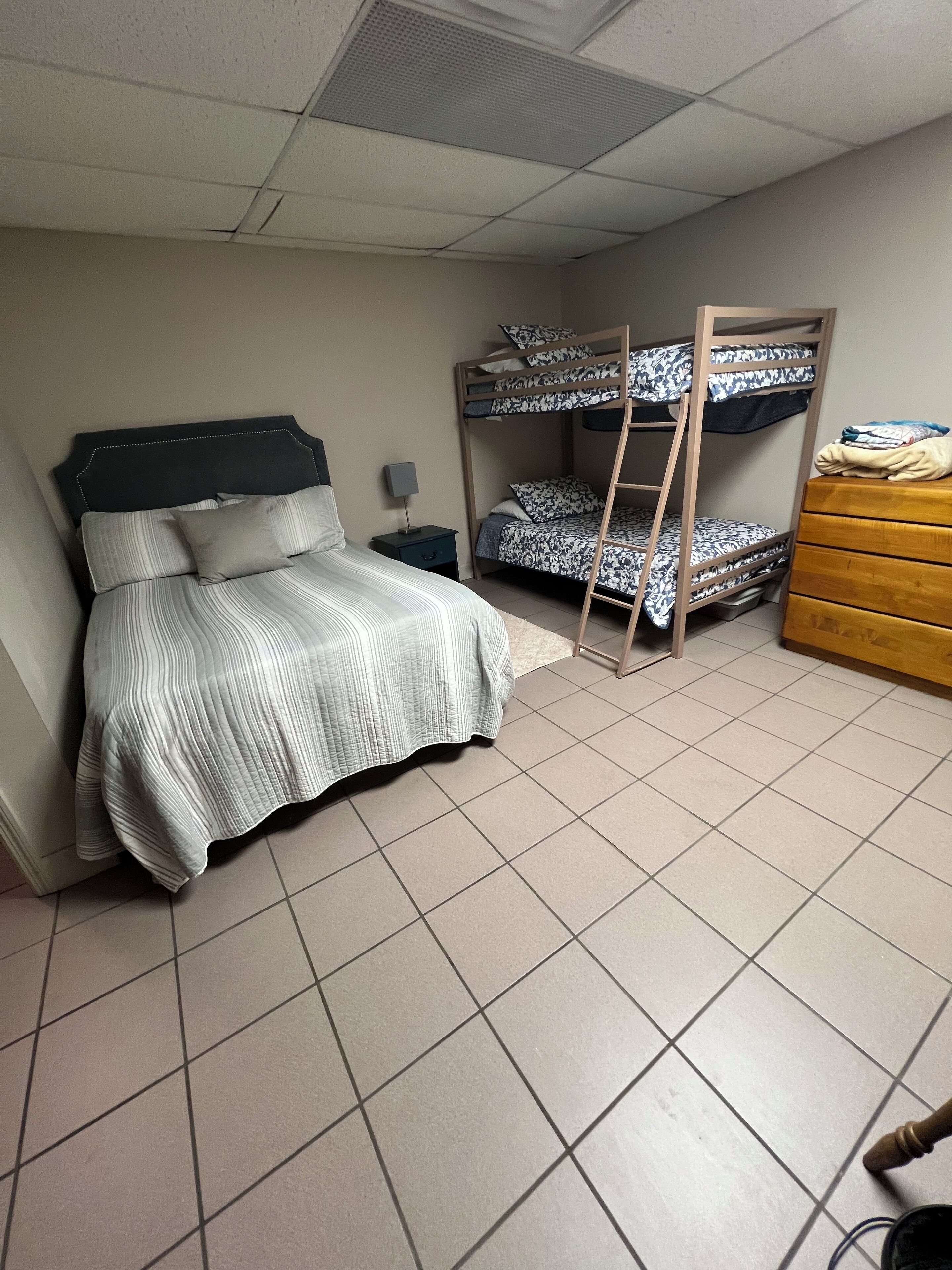 Une chambre avec un lit simple, un lit superposé, une commode et une table de chevet.
