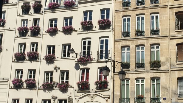 Un immeuble à plusieurs étages, doté de balcons ornés de jardinières fleuries, d’une porte rouge et d’une enseigne bien visible indiquant « Relais Saint-Germain ».