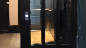 Une porte d’ascenseur noire avec un panneau en verre, un panneau de commande et un plancher en bois.