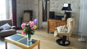 Un salon avec un mur en pierre, une table basse en bois, un fauteuil beige, un canapé et un vase de fleurs.