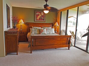 Un dormitorio con una cama de madera, dos mesitas de noche con lámparas, un ventanal con vistas y un ventilador de techo.