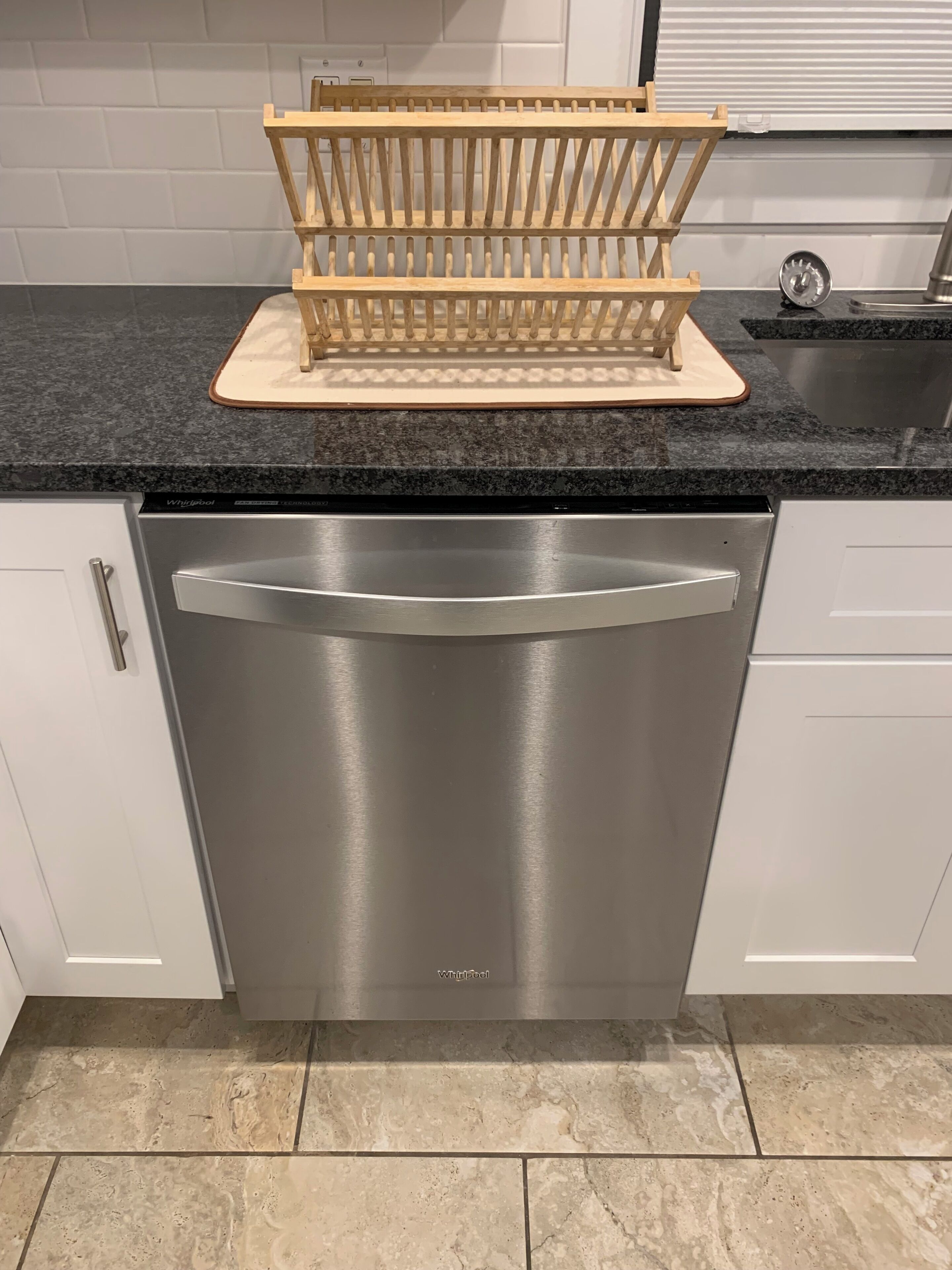 A modern kitchen with a stainless steel dishwasher, white cabinets, and a granite countertop.