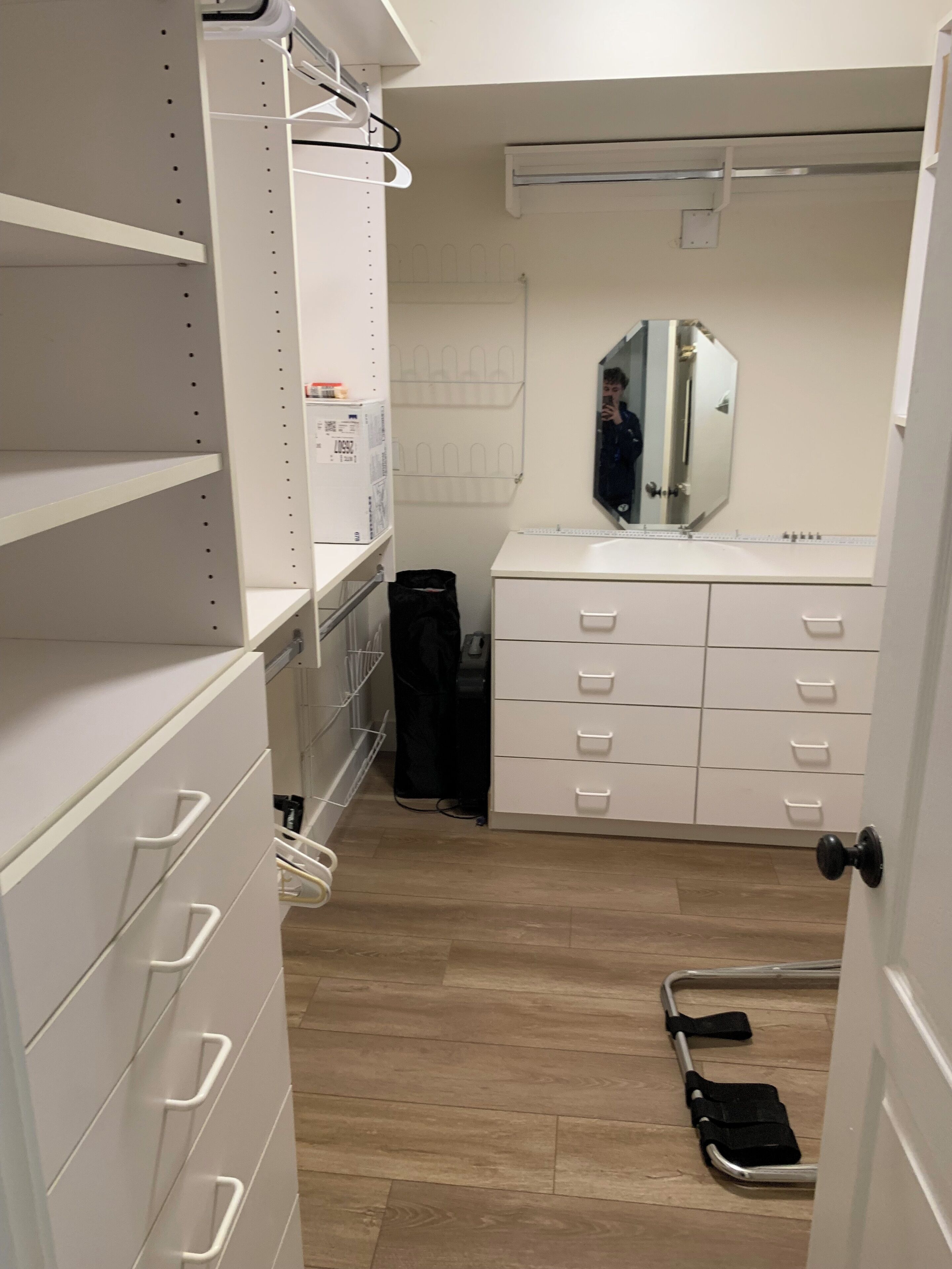 A walk-in closet with white shelving, a mirrored vanity, and a wheelchair in the corner.