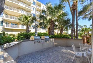 Une terrasse extérieure avec un barbecue, des chaises blanches et un bâtiment avec des balcons en arrière-plan.