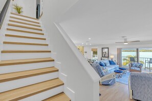 A staircase with wooden steps leading to a living area with a blue sofa, wicker chairs, and a view of the water. - Rx: Paradise updated 2bed/2.5bath townhouse style condo with open water views, shared pool & dockage (Marathon)