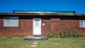 Ein Holzhaus mit weißer Tür, einer kleinen Veranda und einem grünen Dach.