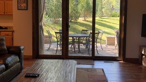 Ein Wohnzimmer mit Couchtisch aus Holz, Ledersofa und einer Schiebetür zu einer Terrasse mit Essplatz.