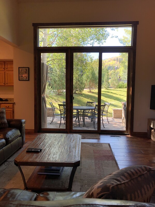 A living room with a wooden coffee table, leather sofa, and a sliding glass door leading to an outdoor patio with a dining set.