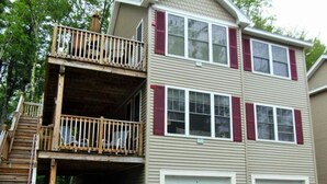 Ein zweistöckiges Haus mit einer Holzterrasse, einer Garage und einem überdachten Patio.