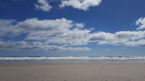 Ein Strand mit breitem Sandstrand und einem klaren Himmel mit vereinzelten Wolken.
