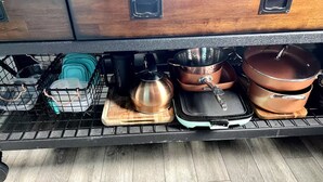 A kitchen with a wooden countertop, a black wire rack, and various kitchenware including pots, pans, and a kettle.