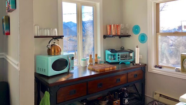 A kitchen with a teal microwave, a toaster oven, and a wooden cutting board.
