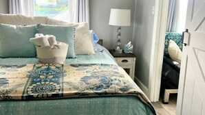 A bedroom with a bed, a bedside table, a lamp, a window with curtains, and a door.