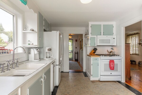 A compact kitchen with white cabinets, a microwave, a stove, and a coffee maker.