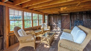 A rustic wooden interior with wicker furniture, large windows, and a fireplace. - Timeless Days, Oceanfront Fisherman’s Cottage, Deep Water Dock & Boathouse (Port Clyde)