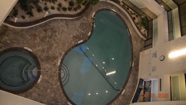 Piscina interior com duas áreas distintas, rodeada por um espaço ajardinado com plantas.
