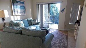 Sala de estar com sofá, luminária, quadro e vista para o exterior por uma porta deslizante.