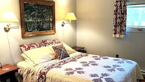 Ein Schlafzimmer mit einem Bett, zwei Nachttischlampen, einem Deckenventilator, einem Fenster mit Vorhängen und einem Bild an der Wand.