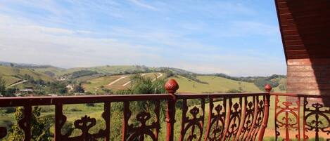 A balcony with ornate wrought iron railings overlooking a rural landscape with rolling hills and a clear sky.