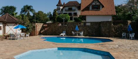A swimming pool area with stone flooring, two lounge chairs, and a table with a blue umbrella.