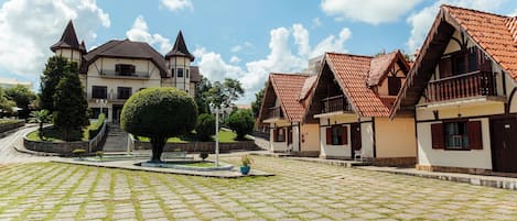 A courtyard with cobblestone paving, traditional European-style buildings with pitched roofs, and a central tree.