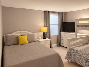 A hotel room with a bed, bedside lamp, TV, dresser, and a window.