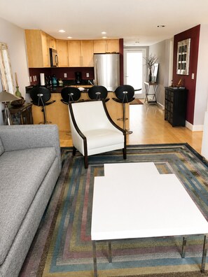 A modern living room with a grey sofa, a white armchair, a coffee table, and a colorful striped rug.