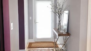 A hallway with a patterned rug, a console table with a vase, and a door with a view to the outside. - Stay in the Heart of Dewey: Beach, Pool & Fun at Your Doorstep (Dewey Beach)